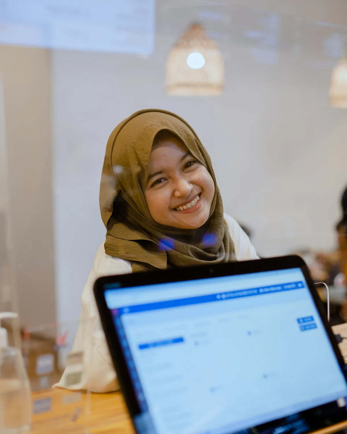 Seorang usahawanita tersenyum sambil bekerja di komputer riba